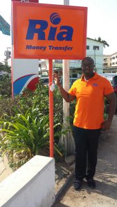 Ria’s Operations Director for Africa, Robert Kotei, displays a newly installed Ria sign in Accra, Ghana│© Ria Money Transfer